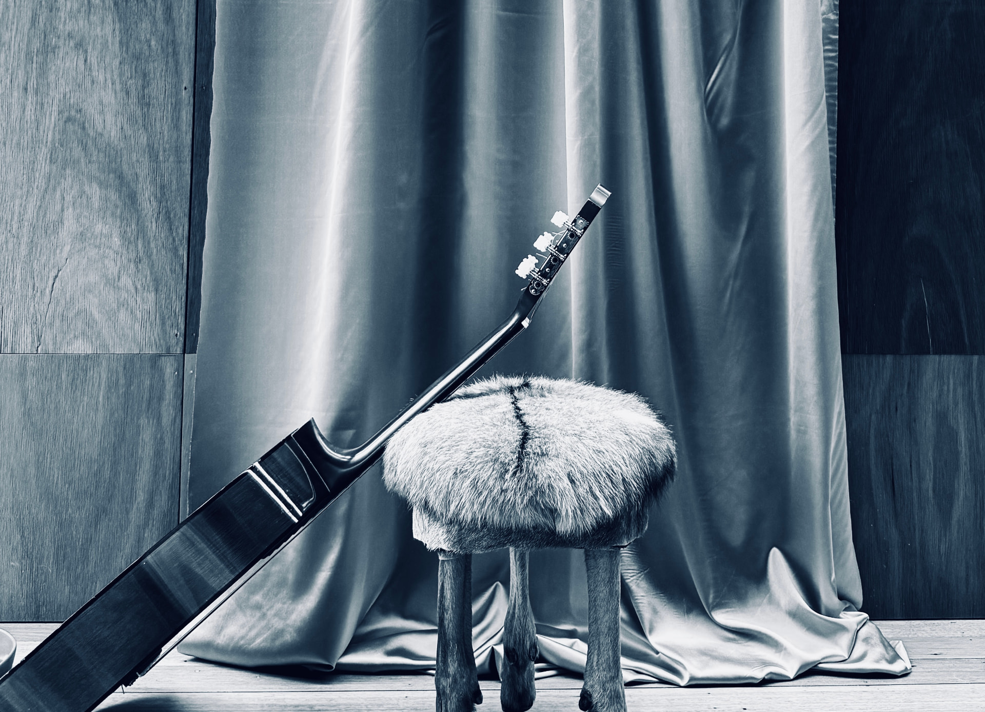A guitar resting on a fur-topped stool in front of draped fabric